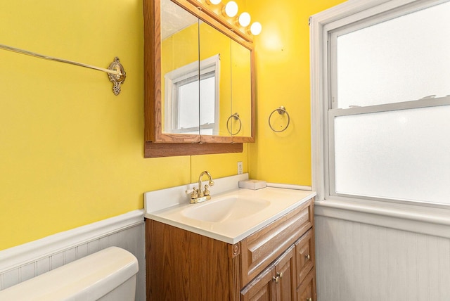 half bath featuring vanity, toilet, and wainscoting