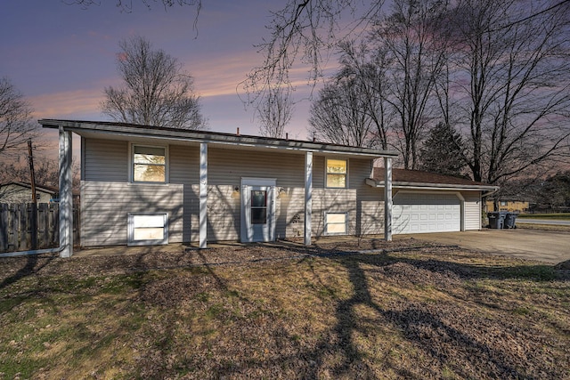 raised ranch featuring a lawn, driveway, a garage, and fence