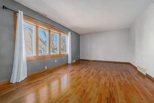 unfurnished room featuring light wood-type flooring, visible vents, baseboards, and a textured ceiling