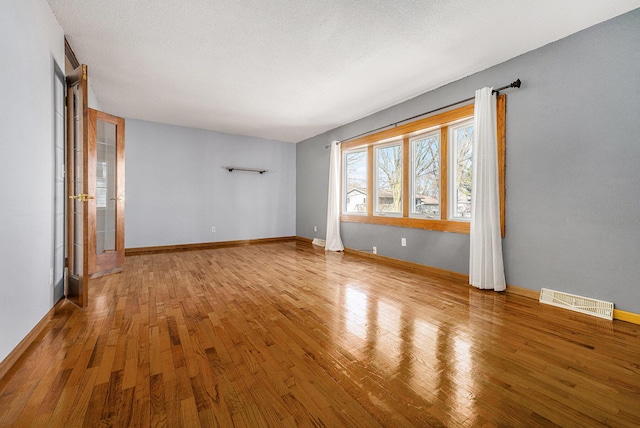 unfurnished room with visible vents, a textured ceiling, baseboards, and hardwood / wood-style floors