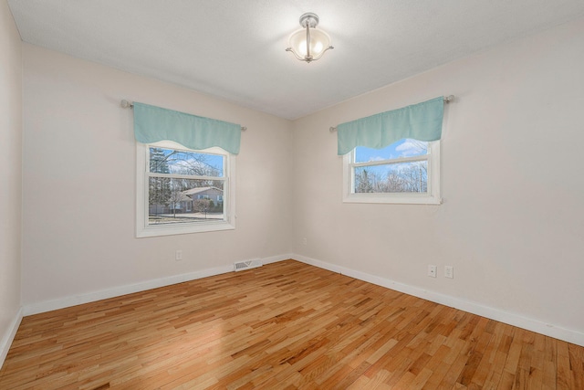 empty room with hardwood / wood-style floors, baseboards, and visible vents