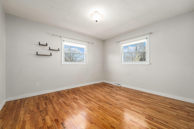 empty room with visible vents, light wood-style flooring, a textured ceiling, and baseboards