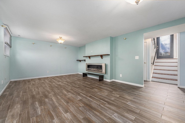 unfurnished living room featuring stairs, baseboards, and wood finished floors