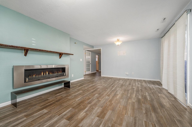 unfurnished living room featuring baseboards, a lit fireplace, and wood finished floors