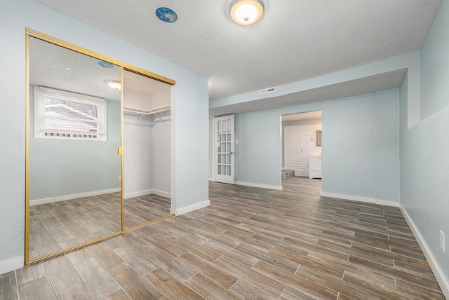 unfurnished bedroom featuring visible vents, baseboards, wood tiled floor, a closet, and a textured ceiling