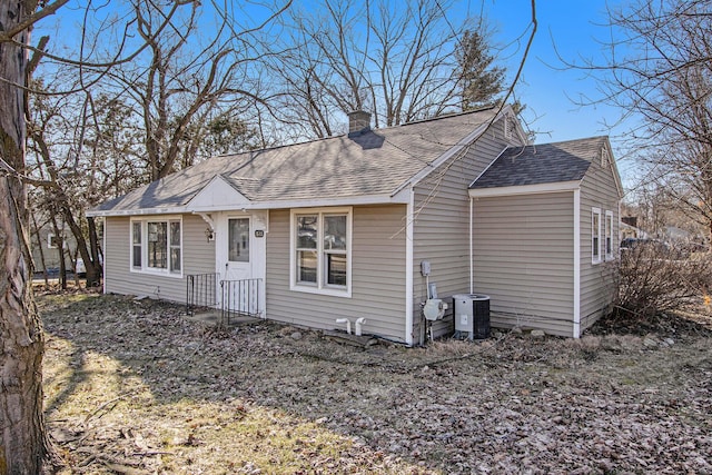 view of front of home featuring cooling unit, roof with shingles, and a chimney