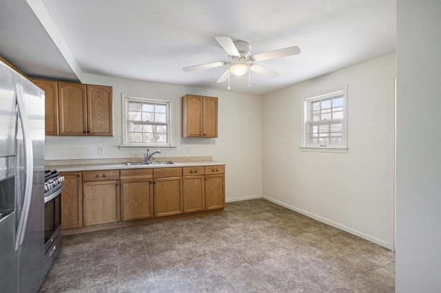 kitchen with brown cabinets, a sink, stainless steel appliances, light countertops, and ceiling fan