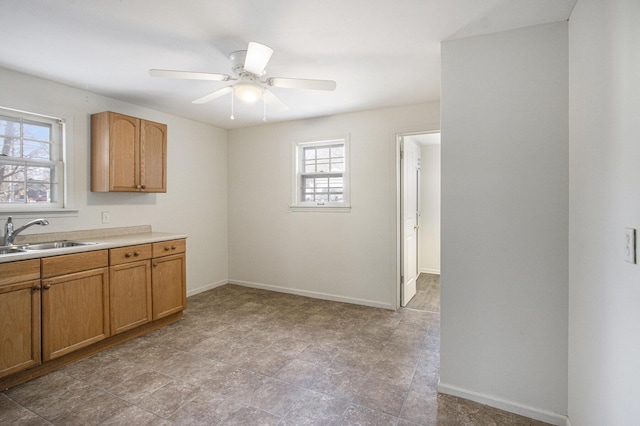 kitchen featuring a ceiling fan, baseboards, a sink, light countertops, and brown cabinets