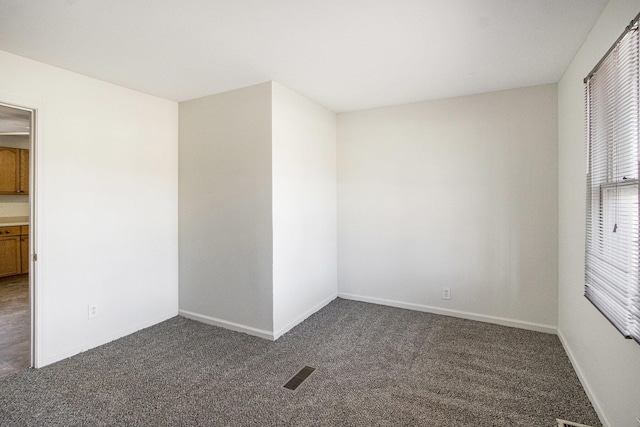 spare room featuring visible vents, dark carpet, and baseboards