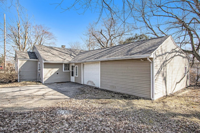 exterior space with an attached garage, a chimney, driveway, and roof with shingles