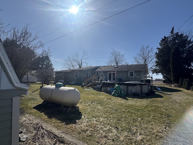 rear view of house with a deck, a covered pool, and a lawn