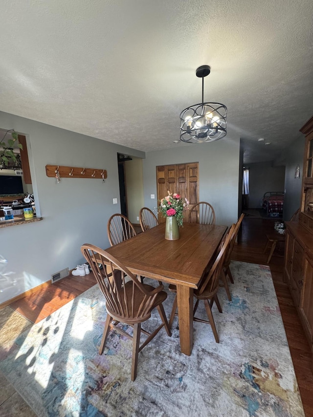 dining space with visible vents, a textured ceiling, an inviting chandelier, and wood finished floors