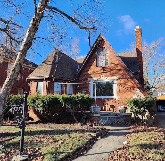 view of front facade with brick siding, a chimney, and a shingled roof