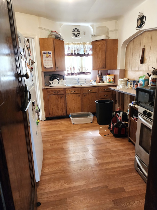 kitchen with brown cabinetry, a sink, black appliances, light countertops, and light wood-style floors