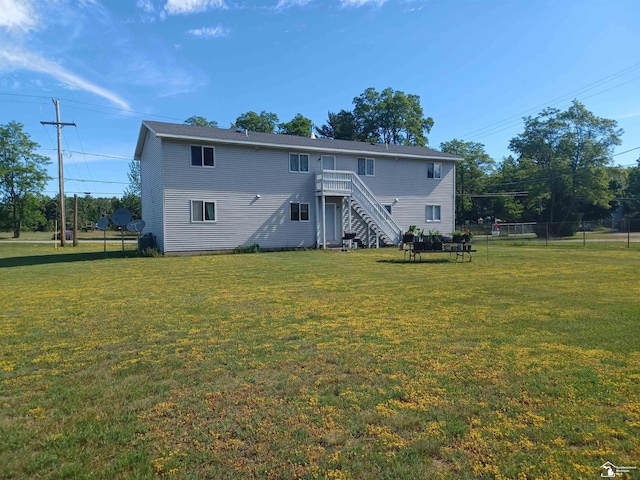 rear view of property featuring stairway, a lawn, and fence