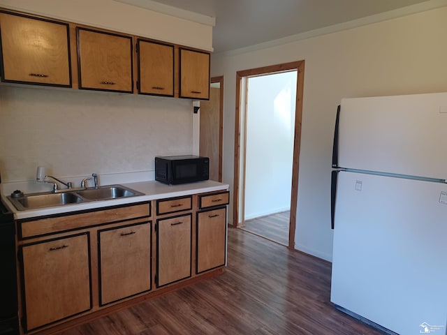 kitchen with black microwave, dark wood finished floors, light countertops, freestanding refrigerator, and a sink