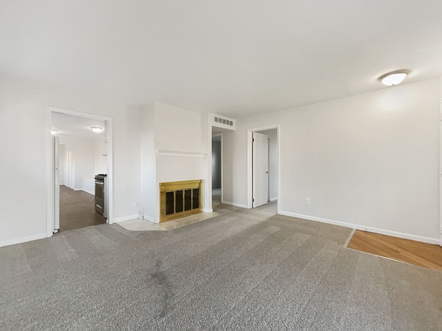 unfurnished living room featuring baseboards, visible vents, a fireplace with flush hearth, and carpet floors