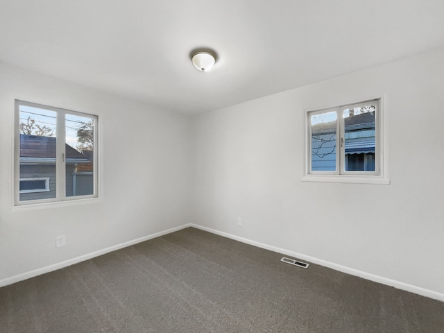 spare room with visible vents, baseboards, and dark carpet