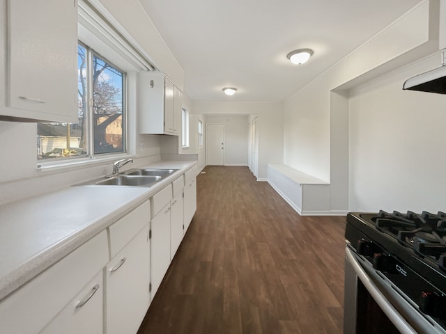 kitchen featuring dark wood-style floors, stainless steel gas range, a sink, light countertops, and white cabinets