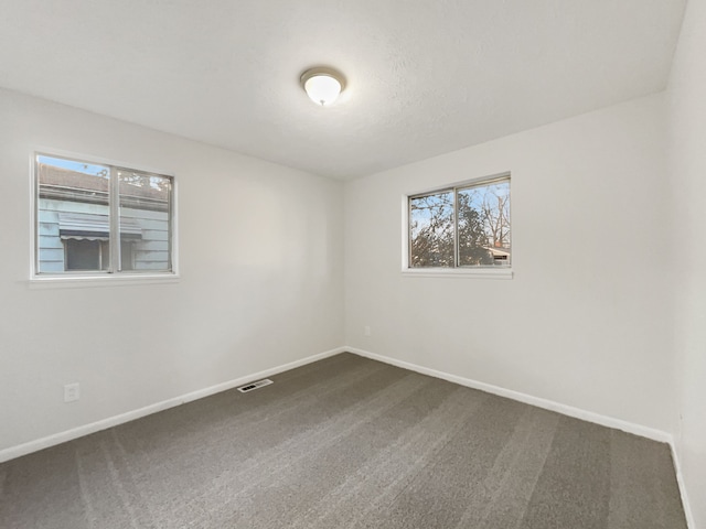 unfurnished room with dark colored carpet, visible vents, and baseboards