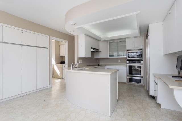 kitchen featuring a sink, under cabinet range hood, appliances with stainless steel finishes, a peninsula, and light countertops