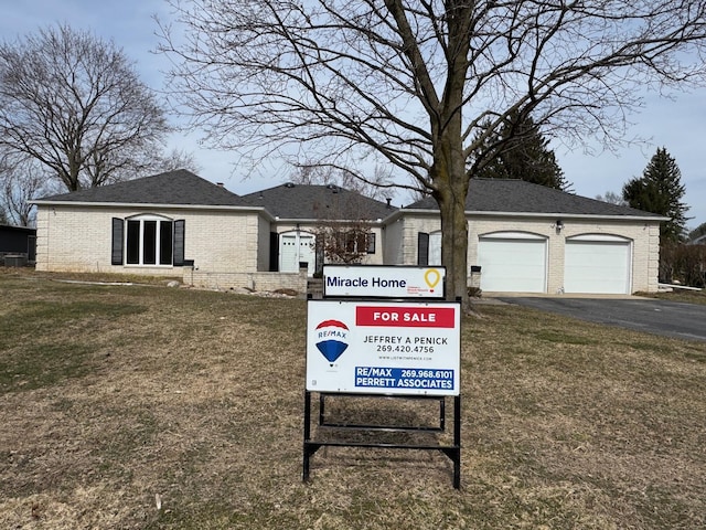 view of front facade featuring aphalt driveway, an attached garage, brick siding, and a front lawn