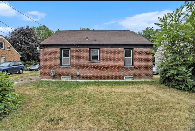 rear view of house with brick siding, a lawn, and roof with shingles