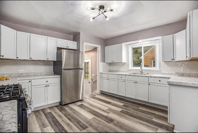 kitchen with a sink, black gas stove, freestanding refrigerator, and wood finished floors