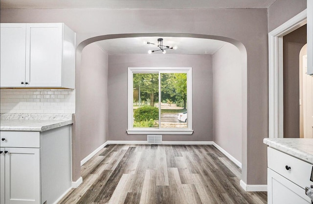 unfurnished dining area featuring visible vents, wood finished floors, arched walkways, an inviting chandelier, and baseboards