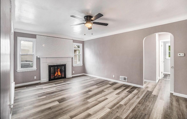 unfurnished living room with wood finished floors, a ceiling fan, arched walkways, and a healthy amount of sunlight