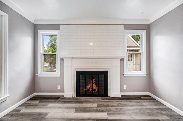 unfurnished living room featuring a warm lit fireplace, baseboards, and wood finished floors