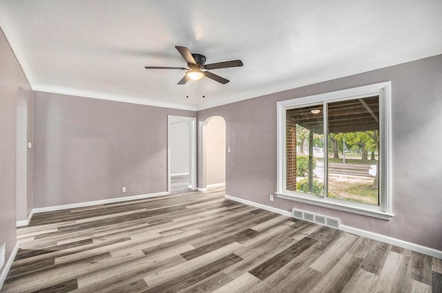 spare room with visible vents, baseboards, ceiling fan, wood finished floors, and arched walkways