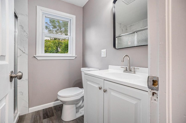 bathroom with vanity, wood finished floors, baseboards, walk in shower, and toilet