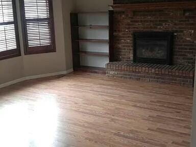 unfurnished living room with a brick fireplace, wood finished floors, and baseboards