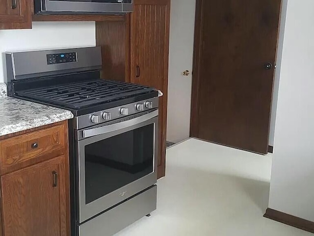 kitchen featuring gas range, brown cabinetry, and light countertops