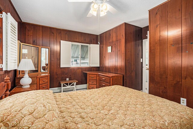 bedroom featuring wood walls, a baseboard heating unit, and a ceiling fan