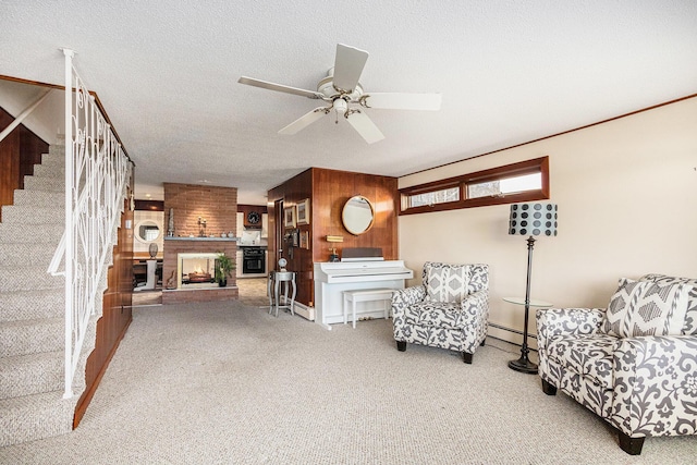 carpeted living room with stairway, a fireplace, ceiling fan, wood walls, and a textured ceiling