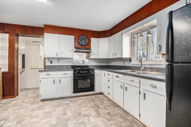 kitchen featuring a sink, under cabinet range hood, dark countertops, freestanding refrigerator, and range