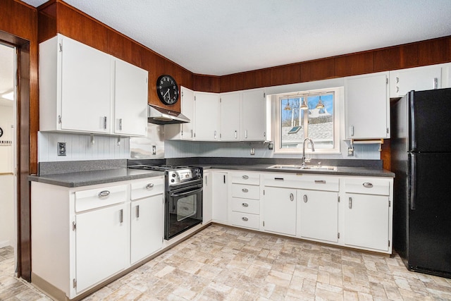 kitchen featuring under cabinet range hood, a sink, dark countertops, freestanding refrigerator, and gas stove