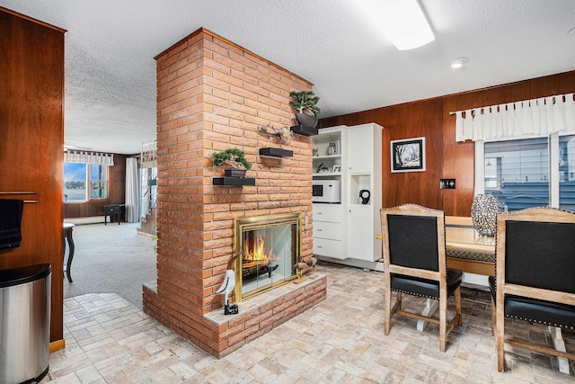 dining area featuring a brick fireplace, a baseboard heating unit, wood walls, brick floor, and a textured ceiling