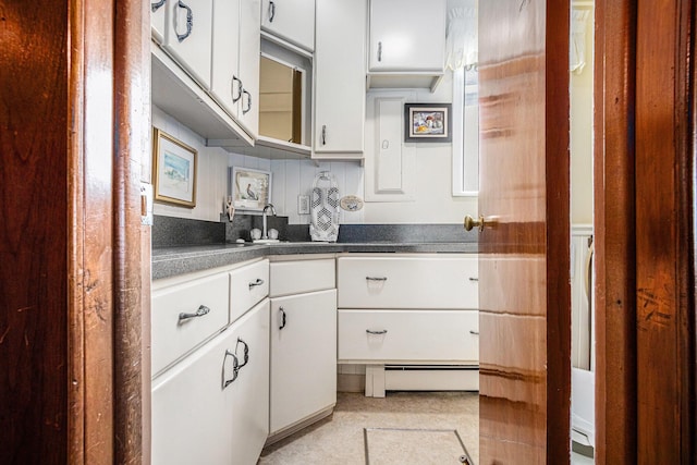 kitchen featuring dark countertops, backsplash, baseboard heating, white cabinetry, and a sink