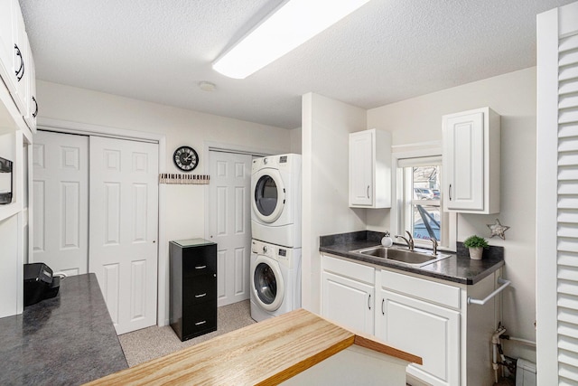 laundry area with a textured ceiling, stacked washer and clothes dryer, and a sink