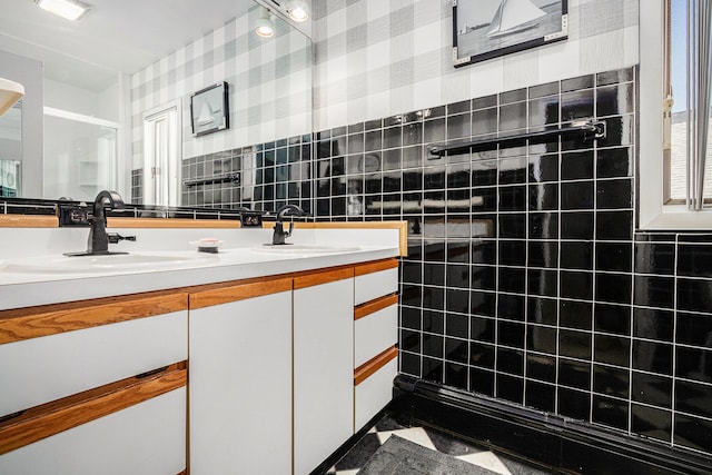 full bath featuring wallpapered walls, double vanity, a tile shower, tile walls, and a sink