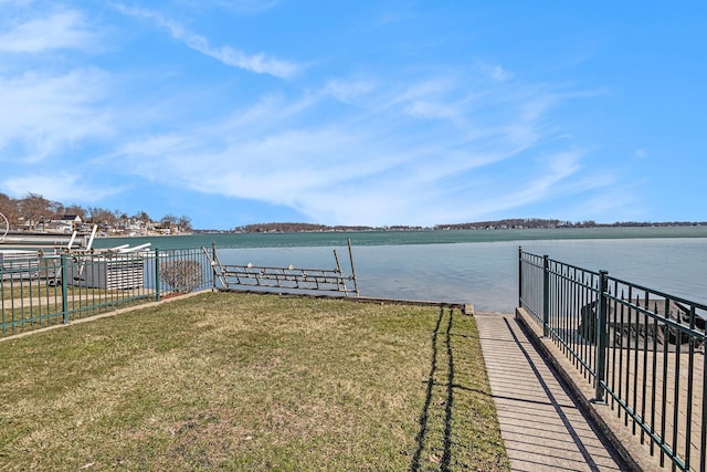 dock area featuring fence, a lawn, and a water view