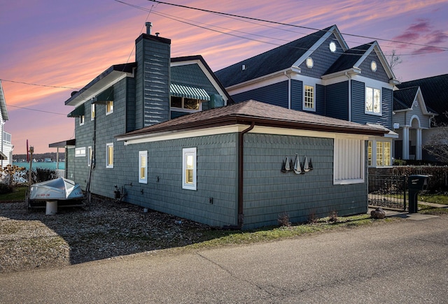 view of side of home with a shingled roof, fence, and a chimney