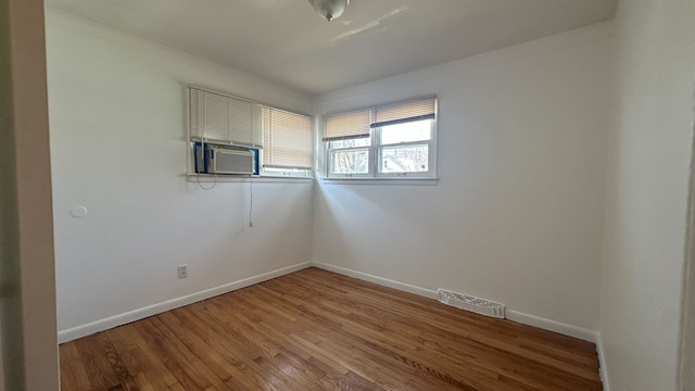 unfurnished room featuring visible vents, wood finished floors, baseboards, and cooling unit