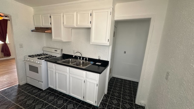 kitchen featuring dark countertops, gas range gas stove, under cabinet range hood, white cabinetry, and a sink