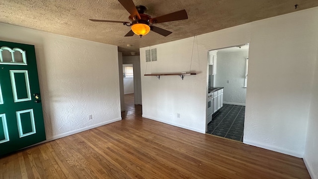 unfurnished room featuring visible vents, dark wood-style flooring, a ceiling fan, and a textured wall