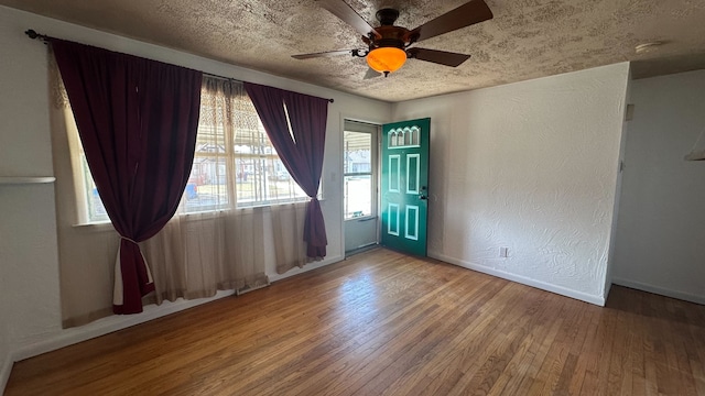 spare room featuring baseboards, ceiling fan, hardwood / wood-style floors, a textured wall, and a textured ceiling