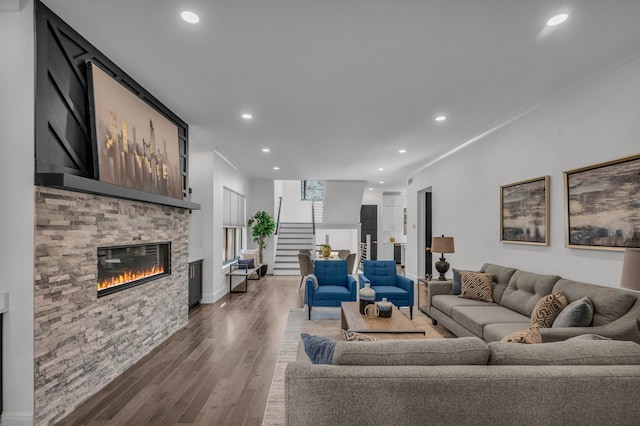 living room with recessed lighting, a stone fireplace, wood finished floors, and stairs